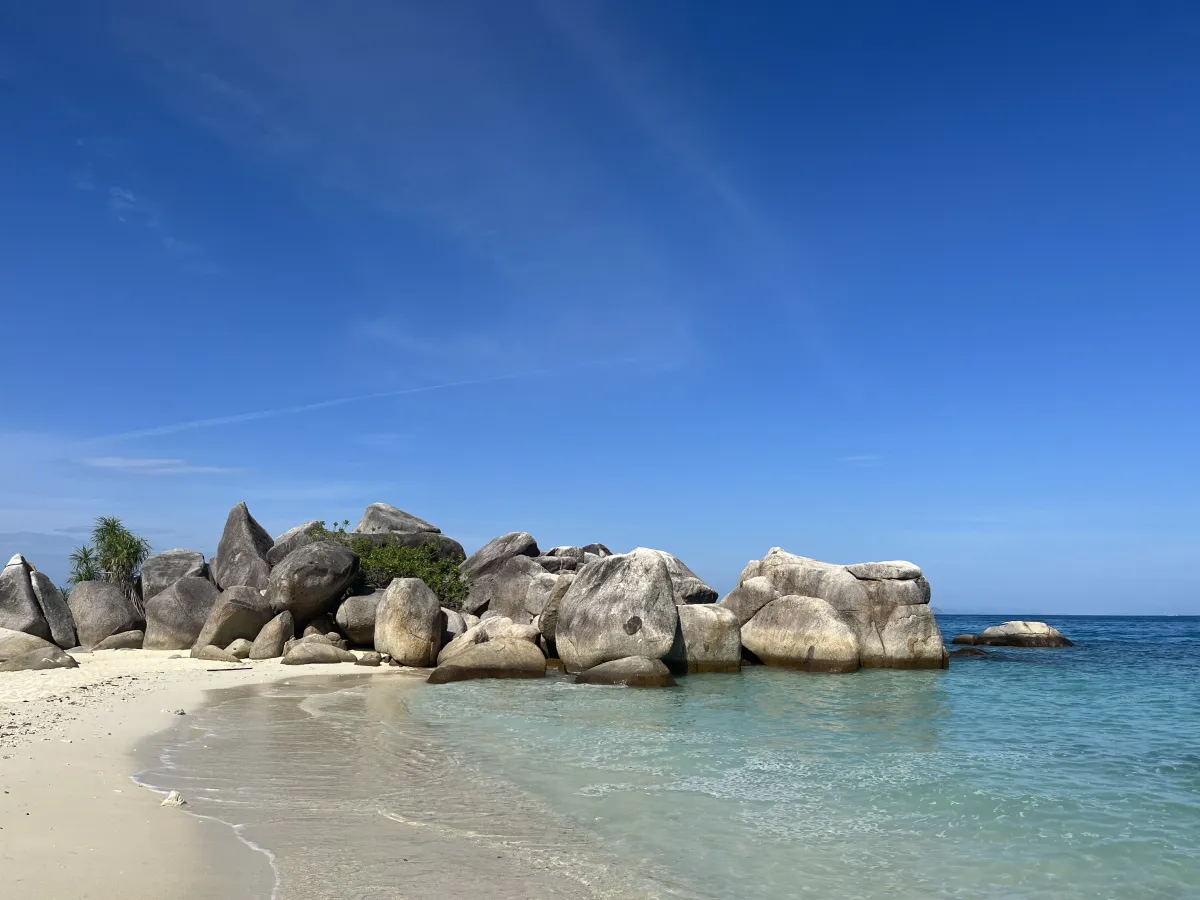 Granite rocks beside a quiet sandy beach and clear blue water.