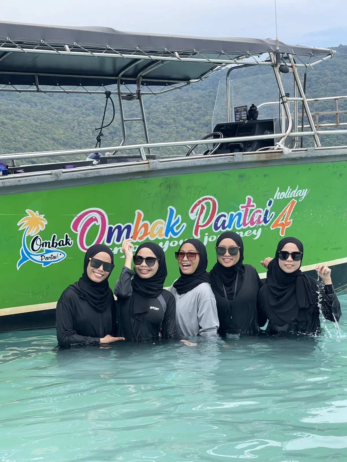 A group beside an Ombak Pantai Holiday boat in shallow water.