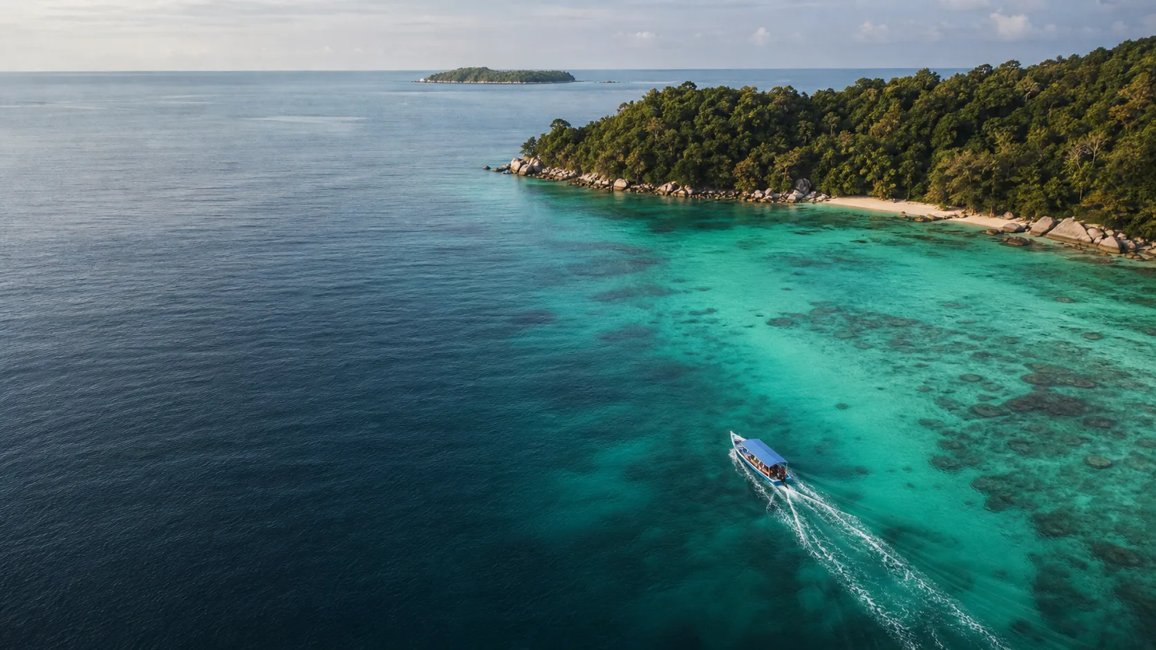 A small tour boat crossing clear water beside a forested Terengganu island.