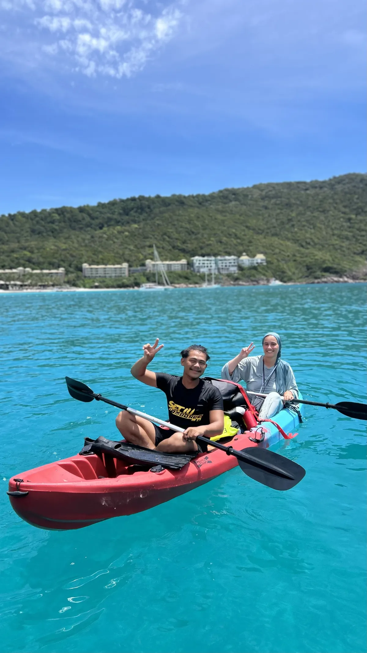 Two people kayaking on clear water near a forested coast.