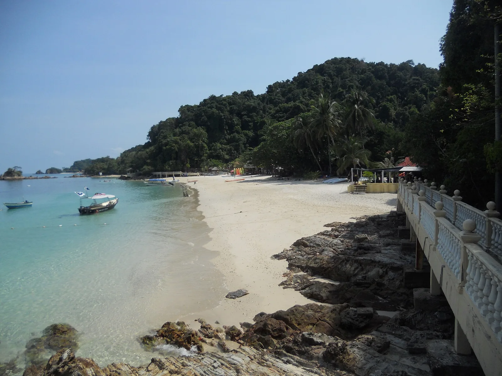 A quiet sandy cove with clear water and forested hills at Kapas Island.