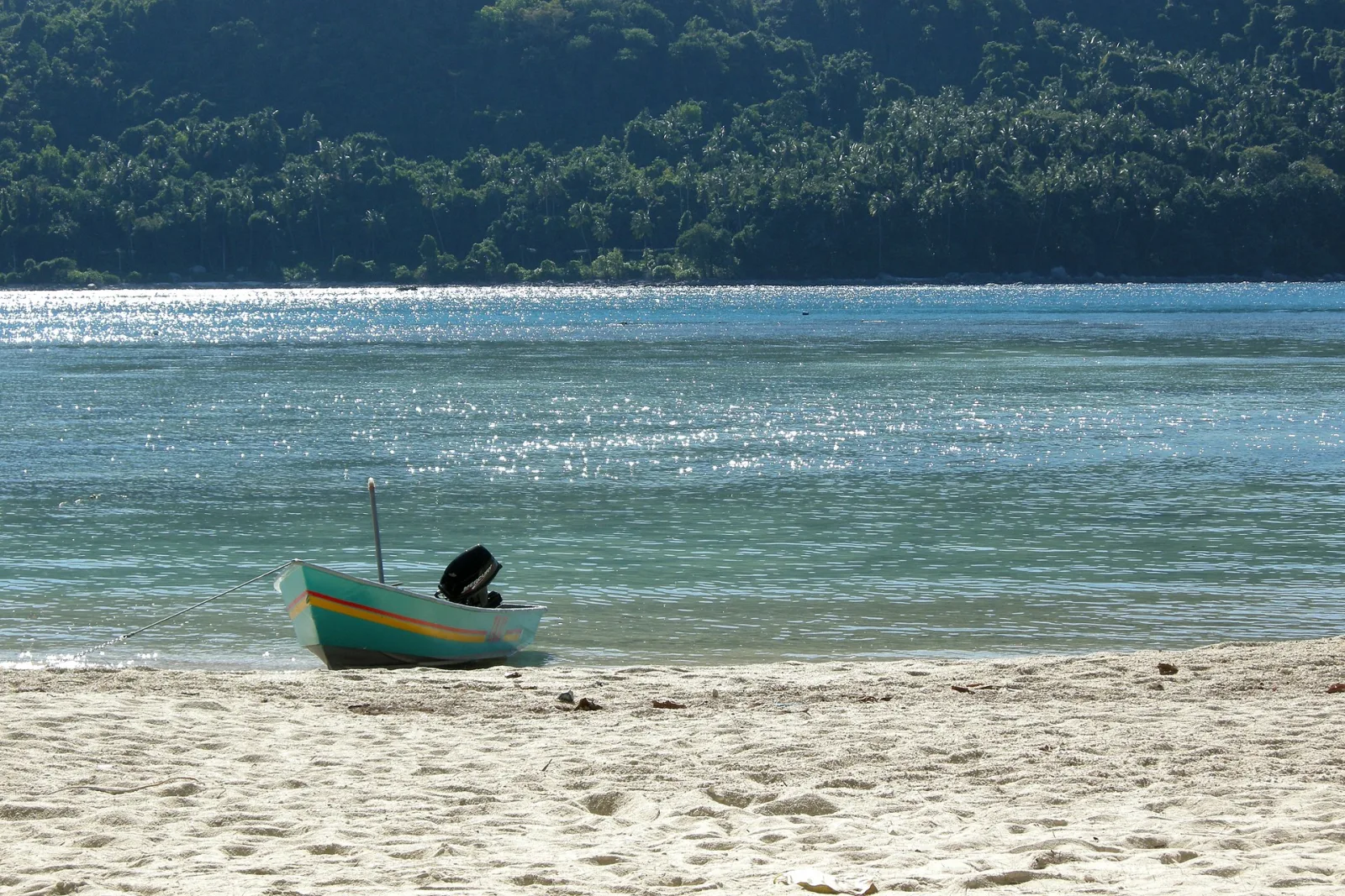 A small boat resting on white sand beside clear water at Perhentian.