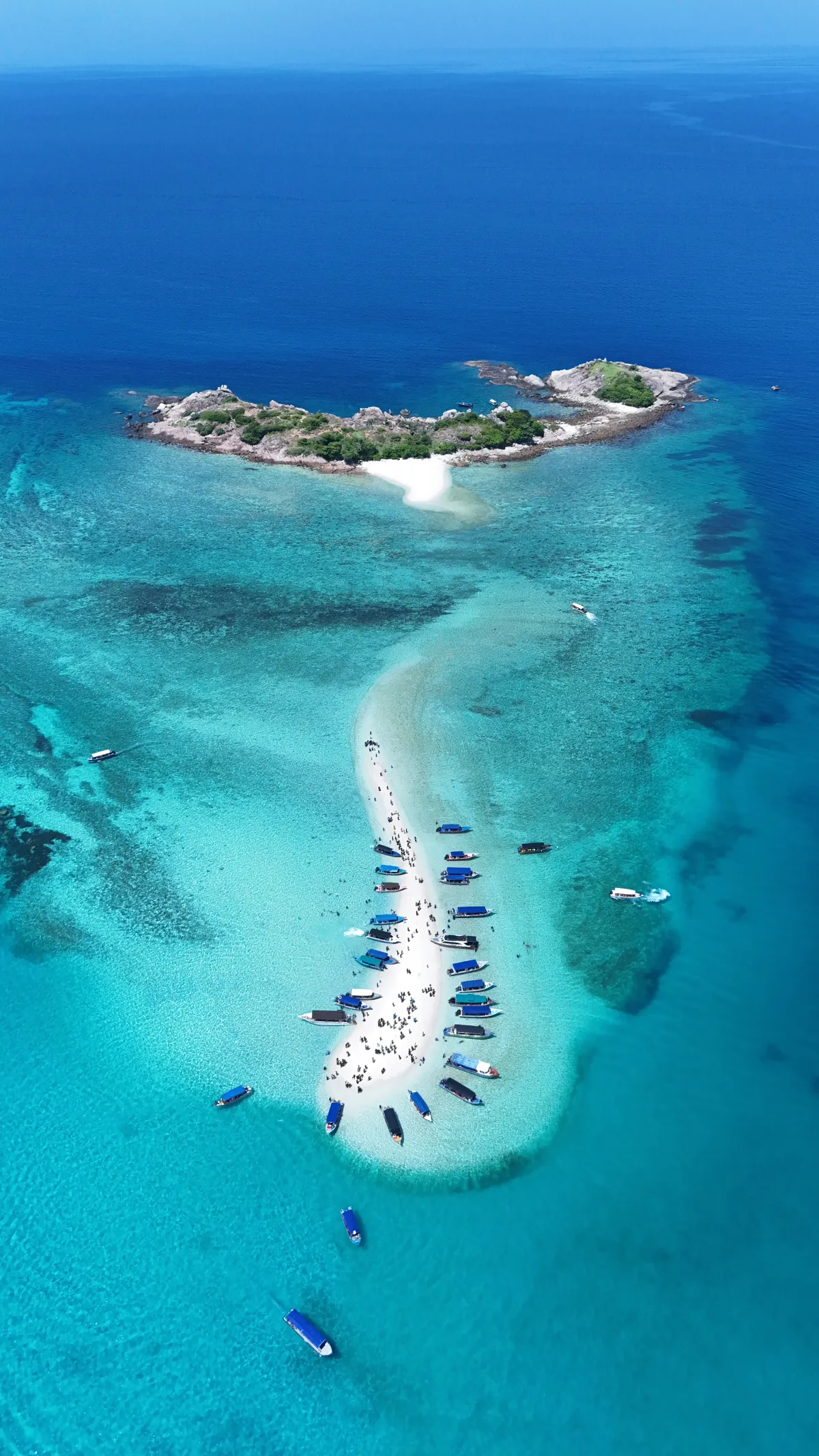 A long sandbank with boats and a small rocky island, seen from above.