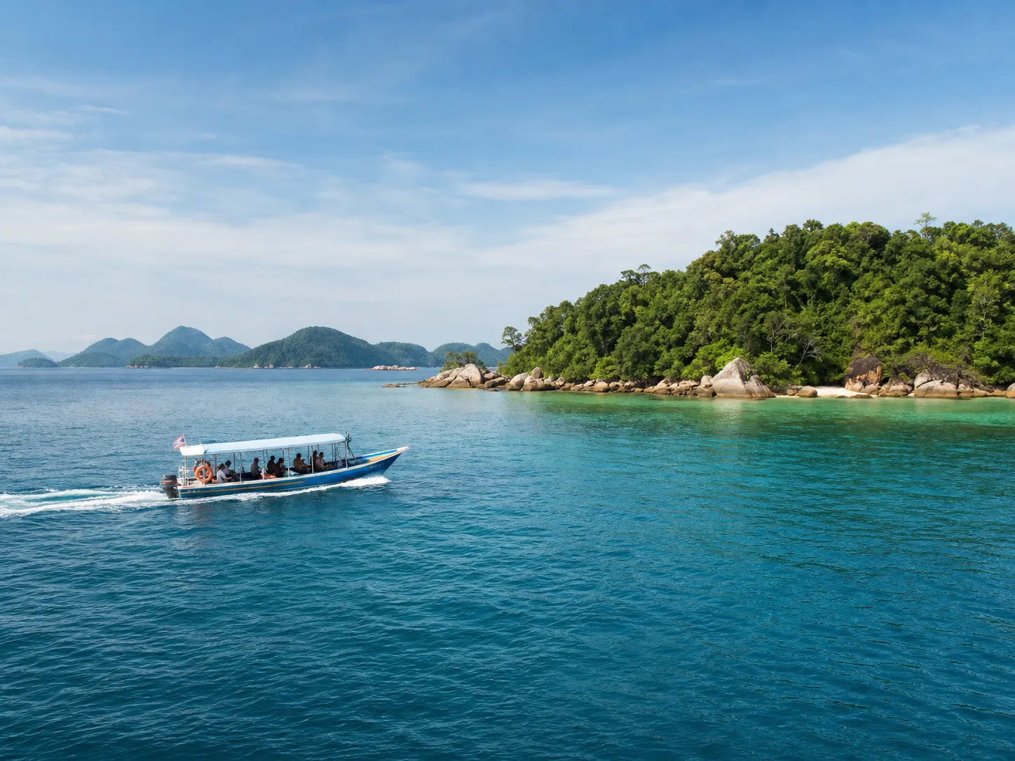 A small passenger boat moving between forested islands.