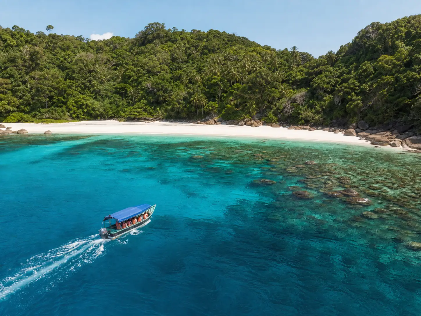 A passenger boat approaching a clear-water island beach.